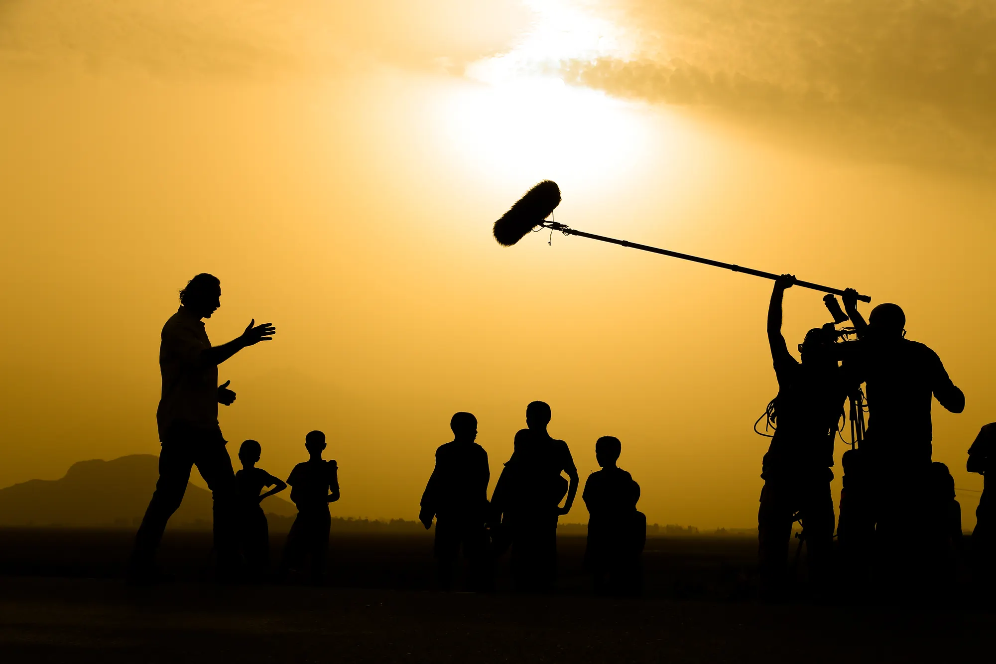 Film crew silhouetted at sunset with a boom microphone, One Call Production on set