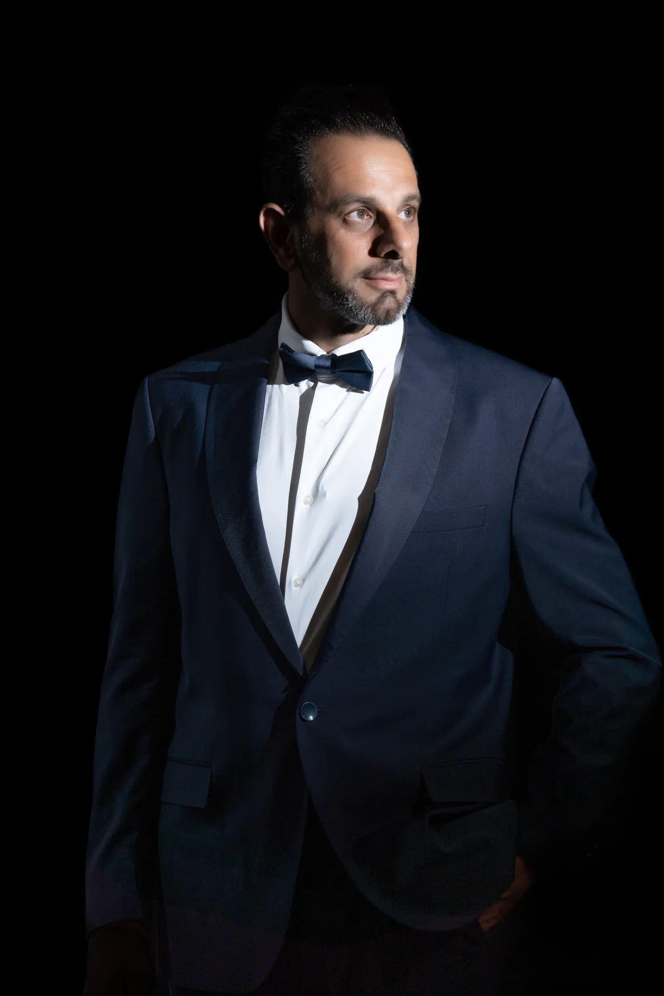 Man in a navy tuxedo on a black background, studio portrait