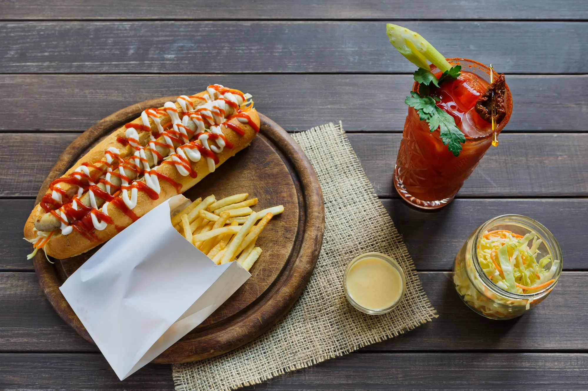Hot dog with fries and a Bloody Mary on a wooden table, restaurant menu photography
