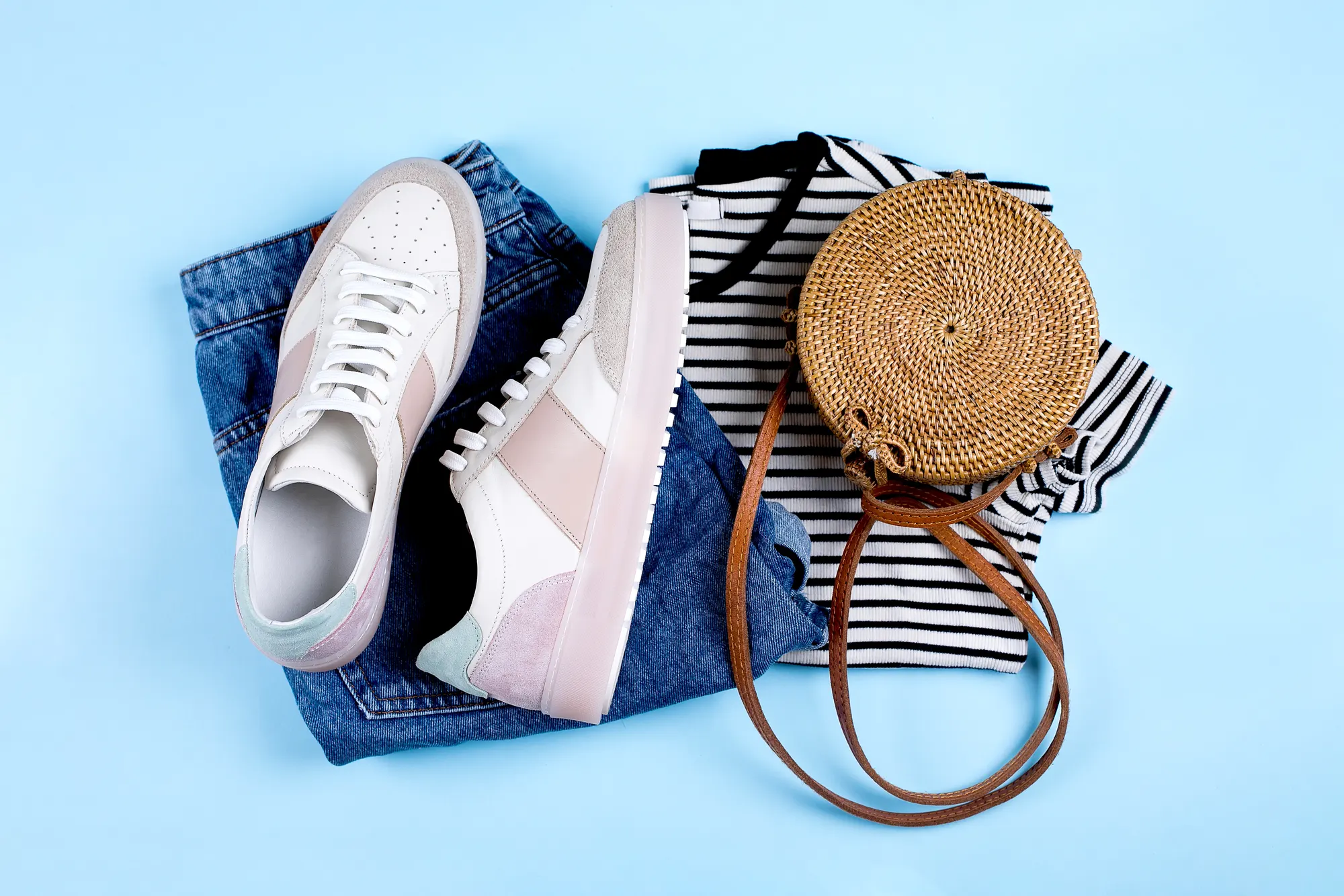 Sneakers, jeans and a rattan bag flat lay on blue, fashion product photo